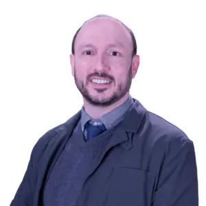 Smiling man with short hair and beard, wearing a grey jacket, sweater, shirt, and tie against a white background.